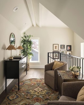 A loft-style living space with a high ceiling, a staircase, a sofa, a coffee table, a side table, a lamp, a plant, and framed pictures on the wall. - Pool, Mini-golf, Sauna, Movie, Gym | Sleep 18 (Austin)