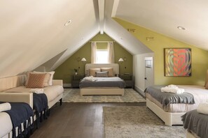 A bedroom with a sloped ceiling, a bed, a sofa, and a bedside table. - Pool, Mini-golf, Sauna, Movie, Gym | Sleep 18 (Austin)