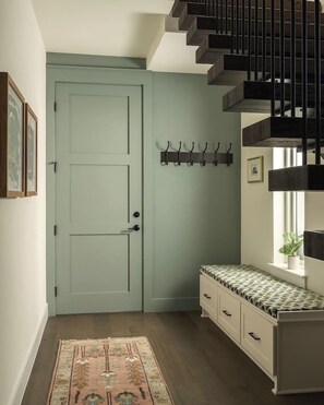 A hallway with a light blue door, a bench with a patterned cushion, and a staircase with dark wood railings. - Pool, Mini-golf, Sauna, Movie, Gym | Sleep 18 (Austin)
