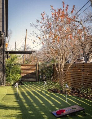 A backyard with artificial grass, a wooden fence, and a tree with autumn leaves. - Pool, Mini-golf, Sauna, Movie, Gym | Sleep 18 (Austin)