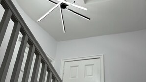Um ventilador de teto moderno com design em forma de estrela, uma porta branca e uma escada com corrimão de madeira.
