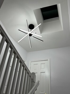 Ein moderner Deckenventilator mit Sternenmuster, eine weiße Tür und eine Treppe mit Holzhandläufen.