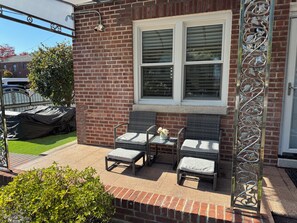 A patio with two wicker chairs and a small table, a brick wall, and a metal decorative panel.