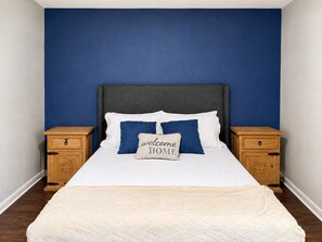 Ein Schlafzimmer mit einem Bett, zwei Nachttischen und einer blauen Wand.