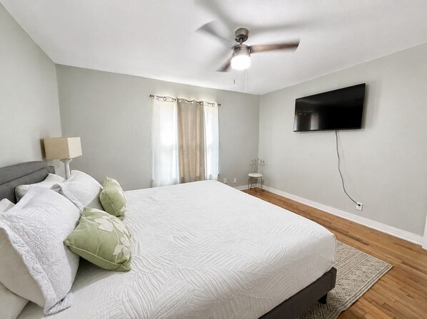 A bedroom with a bed, a ceiling fan, a TV mounted on the wall, and a window with curtains. - Family-Friendly 3BR – 1 Mi to Six Flags, AT&T Stadium & Globe Life Field (Arlington)