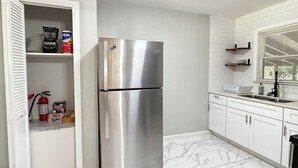 A kitchen with a stainless steel refrigerator, white cabinets, a marble floor, and a window with blinds. - Family-Friendly 3BR – 1 Mi to Six Flags, AT&T Stadium & Globe Life Field (Arlington)