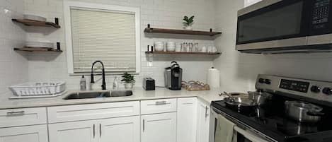 A kitchen with white cabinets, a stainless steel stove, a microwave, and a window with blinds.