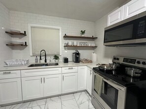 A kitchen with white cabinets, a stainless steel stove, a microwave, and a window with blinds. - Family-Friendly 3BR – 1 Mi to Six Flags, AT&T Stadium & Globe Life Field (Arlington)