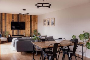Et moderne opholdsrum med en væg i træ, et fladskærms-tv, en sofa, et spisebord med stole og potteplanter.