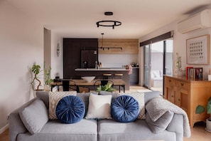 A modern living room with a grey sofa, a dining area, and a kitchen in the background.