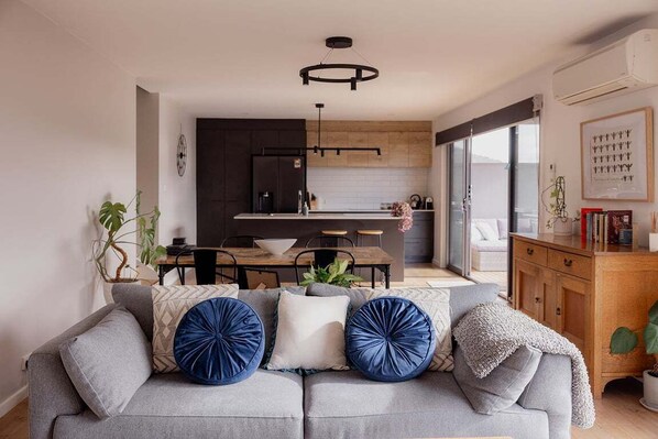 A modern living room with a grey sofa, a dining area, and a kitchen in the background.
