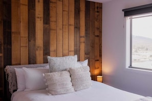 A bedroom with a wooden headboard, white bedding, and a bedside lamp.