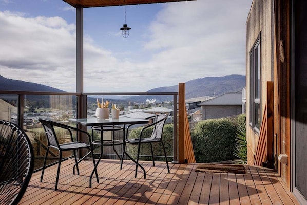 A balcony with a table and chairs, overlooking a mountainous landscape.