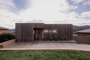 Una casa moderna con techo plano, fachada de madera y un pequeño porche delantero con plantas en macetas.