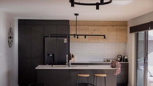 A modern kitchen with a central island, dark cabinetry, and a wooden accent wall.