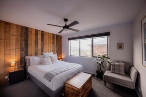 Un dormitorio con una cama, mesitas de noche, ventilador de techo, ventana, planta y un sofá.