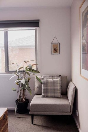 A corner room with a sofa, a potted plant, and a framed picture on the wall.