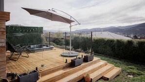 A wooden deck with a hot tub, outdoor seating, and a view of the city.