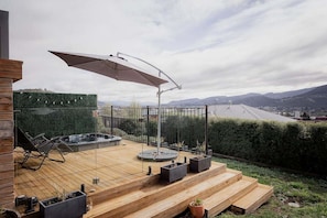 A wooden deck with a hot tub, outdoor seating, and a view of the city.