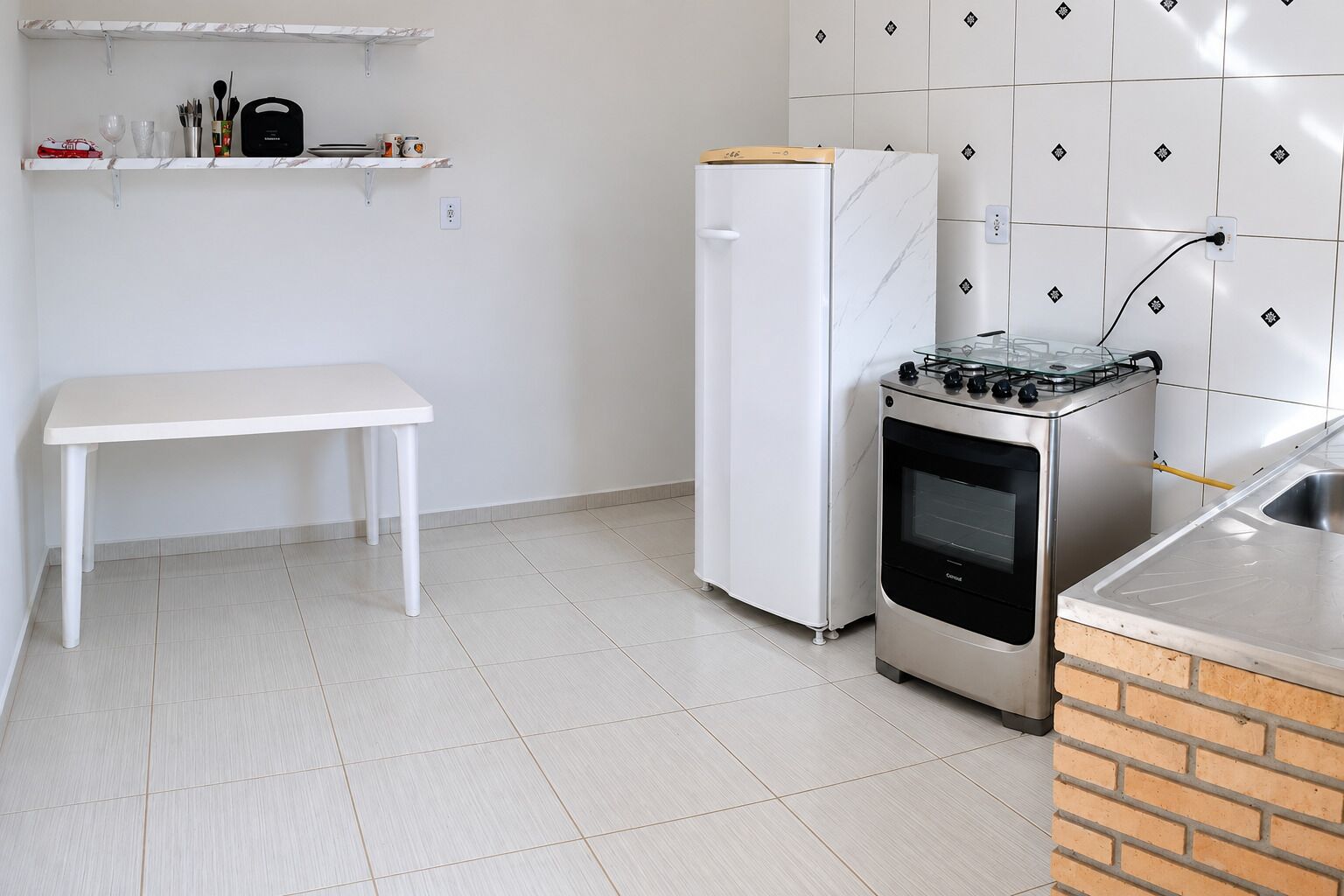 Een compacte keuken met een wit aanrecht, een witte koelkast, een gasfornuis en een bakoven.