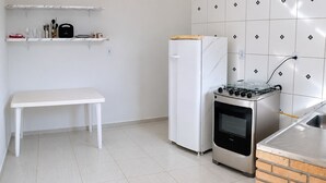 Een compacte keuken met een wit aanrecht, een witte koelkast, een gasfornuis en een bakoven.