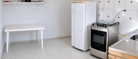 A compact kitchen with a white bench, a white refrigerator, a gas stove, and a brick oven.