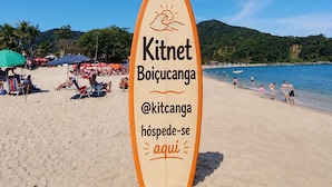 Een surfboard-vormig bord met de tekst 'Kitnet Boicucanga' en een strand in de achtergrond.