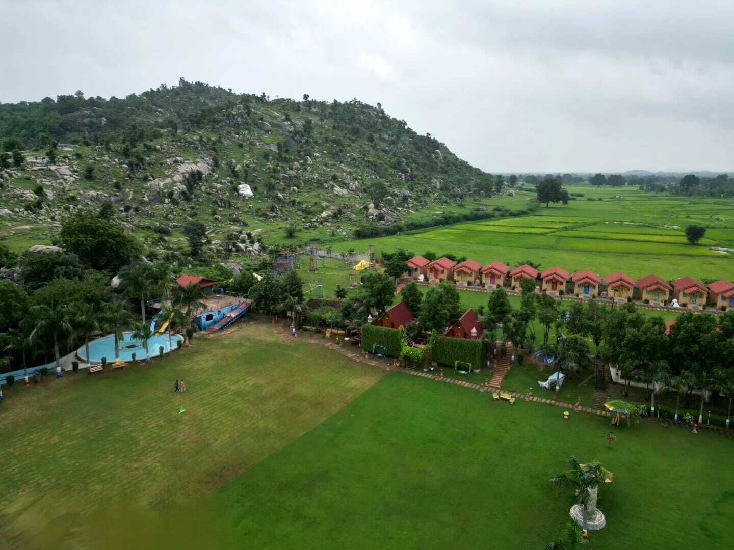 A resort with multiple red-roofed cottages, a swimming pool, and lush green fields.