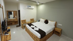 A hotel room with a bed, bedside tables, a desk, a chair, a mirror, and a ceiling fan. - Vatika Green Resort & Restaurant  (Devgadh Bariya)