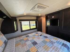 A bedroom with a large bed, a window, a television, and a door.