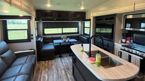 Ein kompaktes Wohnmobil-Interieur mit einer Küchenzeile, einer Sitzecke und einem Fenster mit Blick ins Freie.