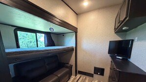 Ein kompaktes Wohnmobil-Interieur mit Etagenbett, kleiner Sitzecke, Fernseher und Küchenzeile.