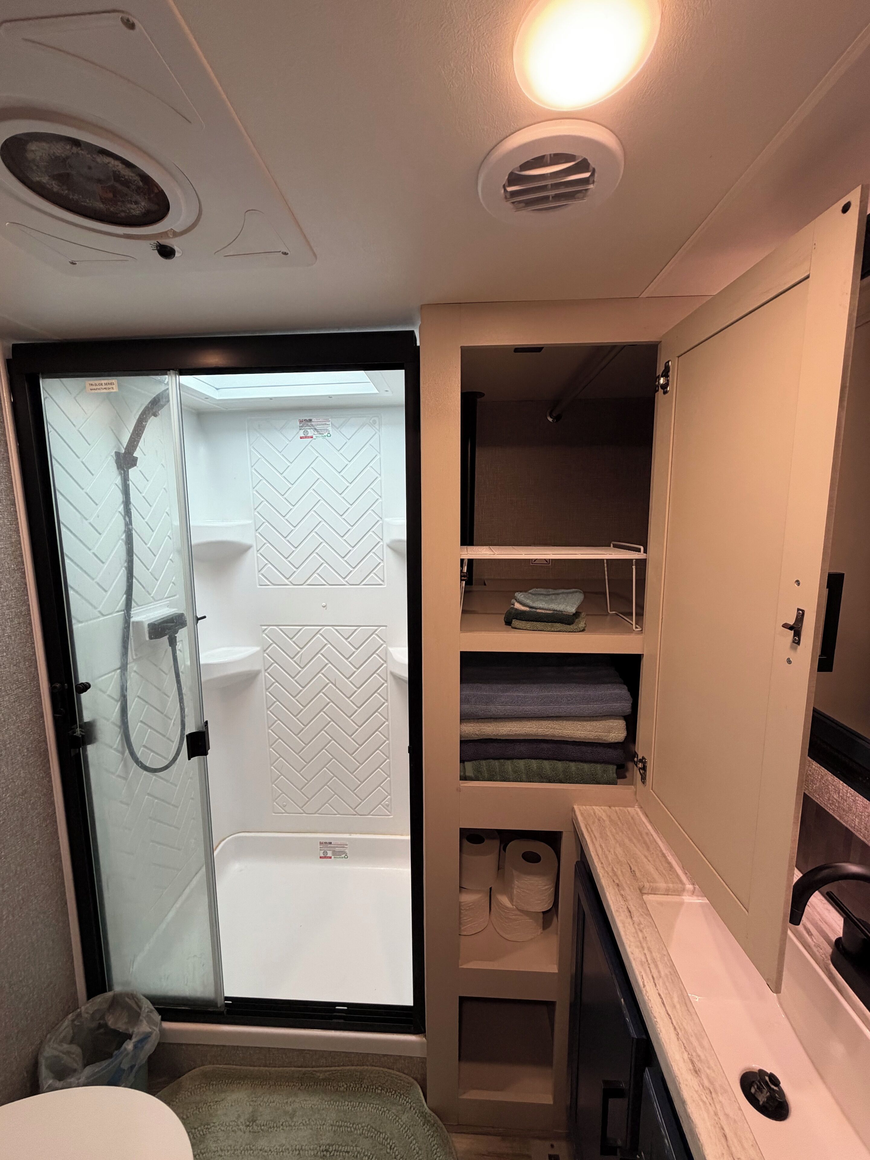 A compact bathroom with a shower, toilet, and storage shelves.
