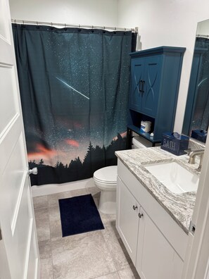 Un baño con cortina de ducha con un cielo estrellado, un inodoro blanco, un armario azul y un lavabo de mármol.