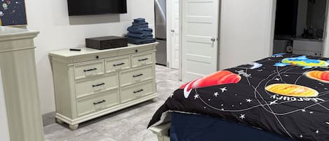 Un dormitorio con cama, cómoda, televisor y ventilador de techo.