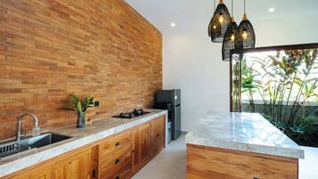 Una cocina moderna con pared de ladrillo, armarios de madera, un lavamanos de acero inoxidable, estufa empotrada y refrigerador.