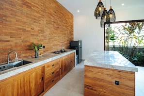 Eine moderne Küche mit Backsteinwand, Holzschränken, einer Edelstahlspüle, einem eingebauten Herd und einem Kühlschrank.