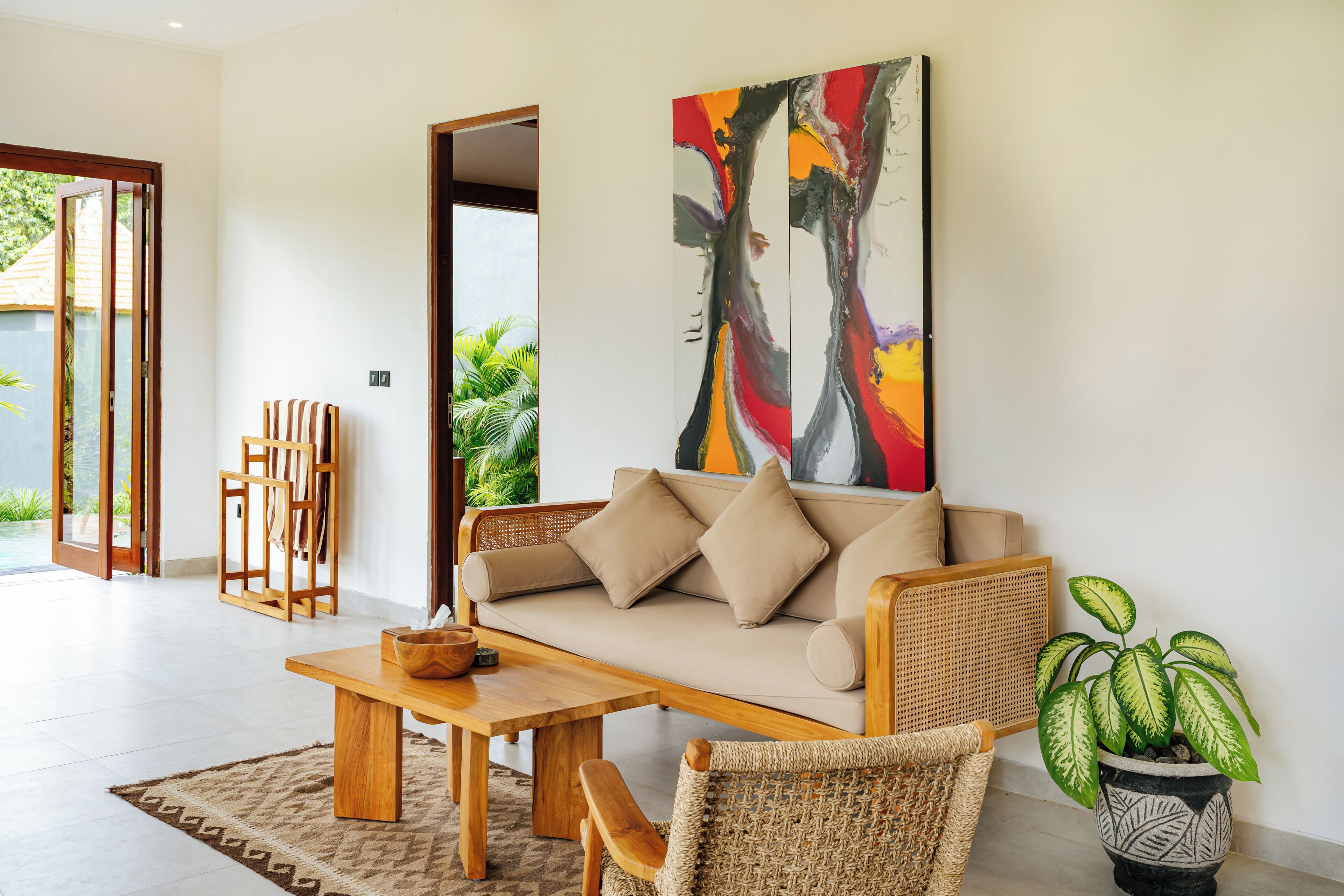 Una sala de estar moderna con sofá, mesa de centro y sillas, un cuadro abstracto de gran tamaño y una planta en maceta.