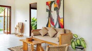 Una sala de estar moderna con sofá, mesa de centro y sillas, un cuadro abstracto de gran tamaño y una planta en maceta.