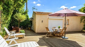 Een houten terras met tuinmeubilair, een overdekte tafel en een parasol.