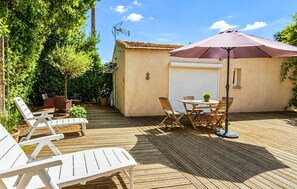 Eine Holzterrasse mit Gartenmöbeln, einem überdachten Tisch und einem Sonnenschirm.