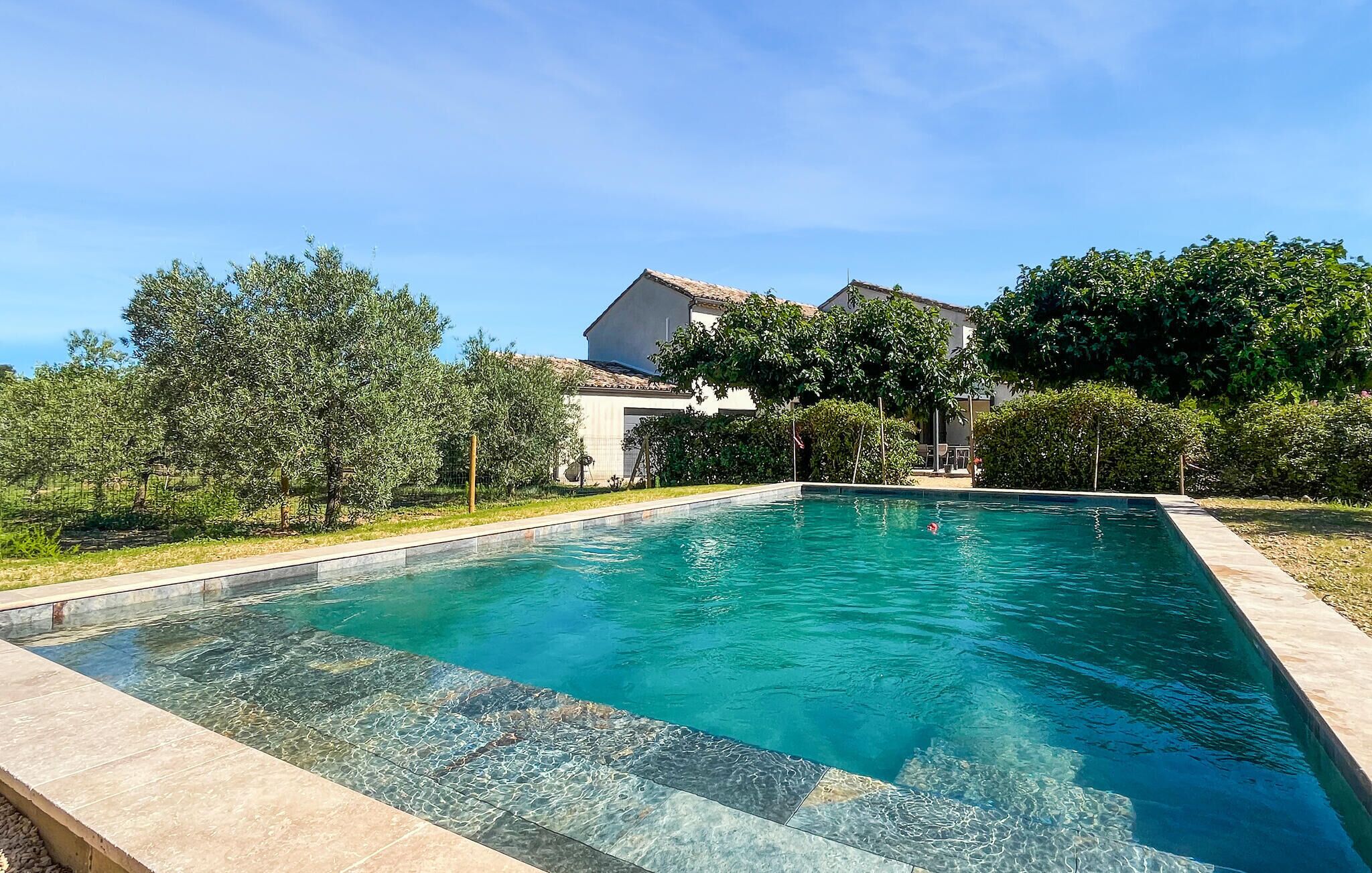 A rectangular swimming pool with clear water, surrounded by a tiled deck and lush greenery.