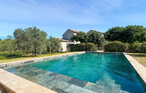 Ein rechteckiger Pool mit klarem Wasser, umgeben von einer gefliesten Terrasse und üppiger Bepflanzung.