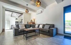 Ein modernes Wohnzimmer mit Ecksofa, Couchtisch, Pendelleuchten und Blick ins Freie.