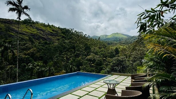 A swimming pool with a view of a lush green landscape and mountains in the background. - Grandlivet Resort (Vythiri)