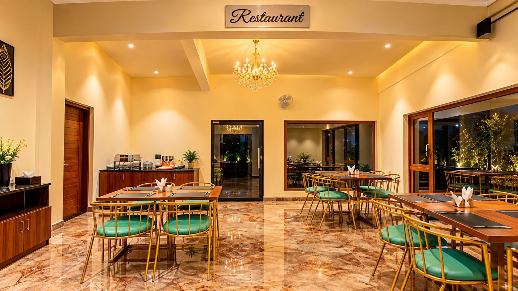 Un restaurante con candelabro, sillas con cojines verdes y piso de mármol.