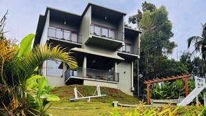 A multi-story building with a balcony on the upper floor, surrounded by lush greenery and a small staircase leading to the entrance. - Grandlivet Resort (Vythiri)