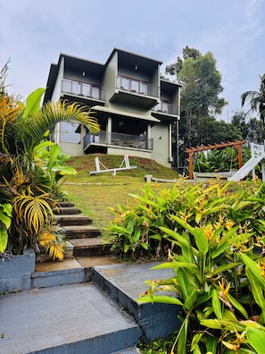 A multi-story building with a balcony on the upper floor, surrounded by lush greenery and a small staircase leading to the entrance. - Grandlivet Resort (Vythiri)