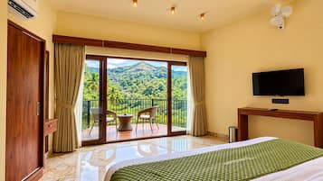 Habitación de hotel con balcón, cama, televisor y vistas a un paisaje montañoso.