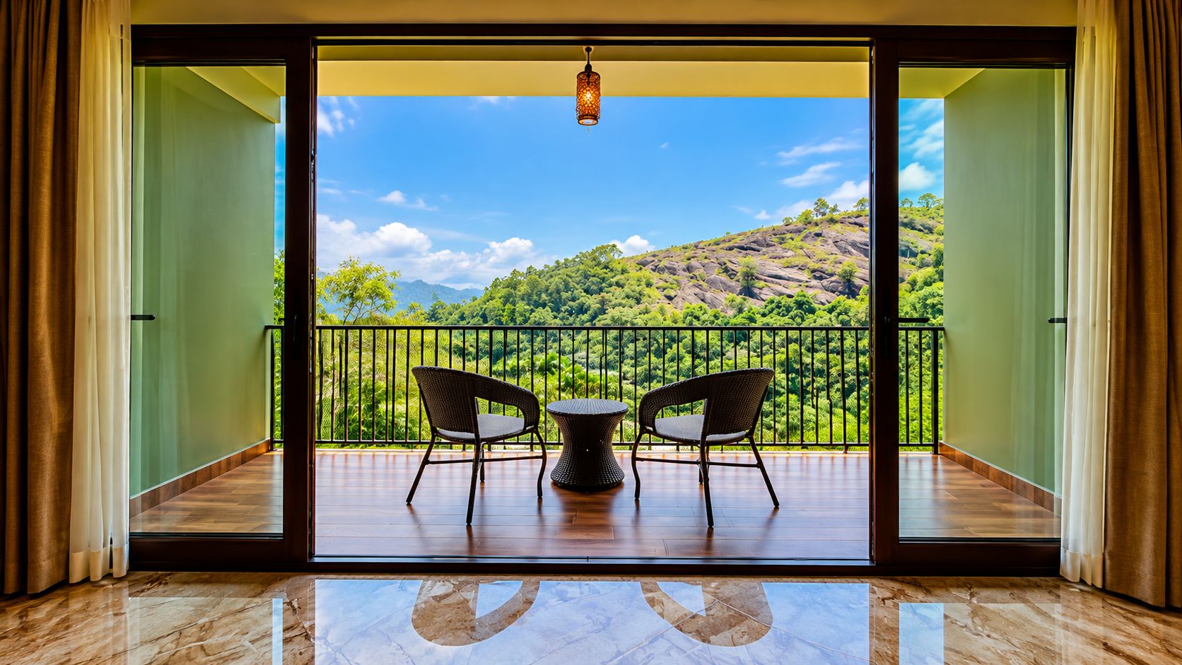 Un balcón con dos sillas de mimbre y una mesa, con vistas a un paisaje verde exuberante y un cielo despejado.